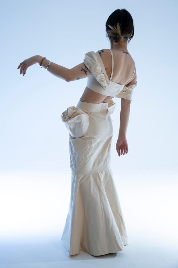 A female model wearing a beige crop top and long skirt, facing away from the camera.